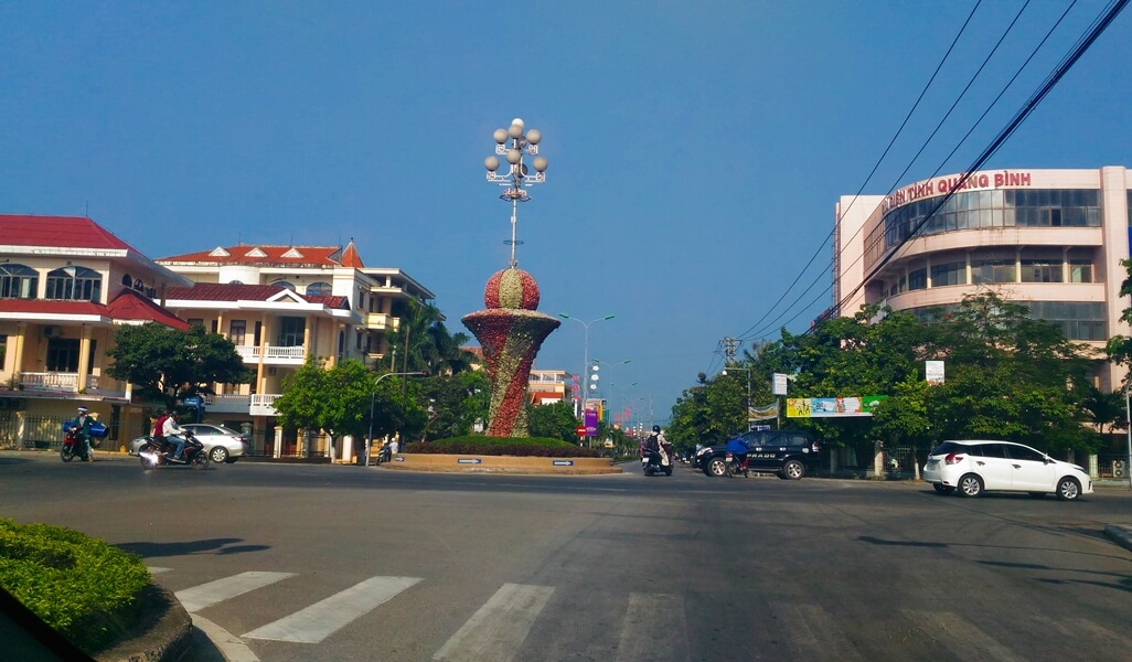 View of a spacious street in downtown Dong Hoi with cars and motorbikes, ideal for exploring the city with a rental car and driver.