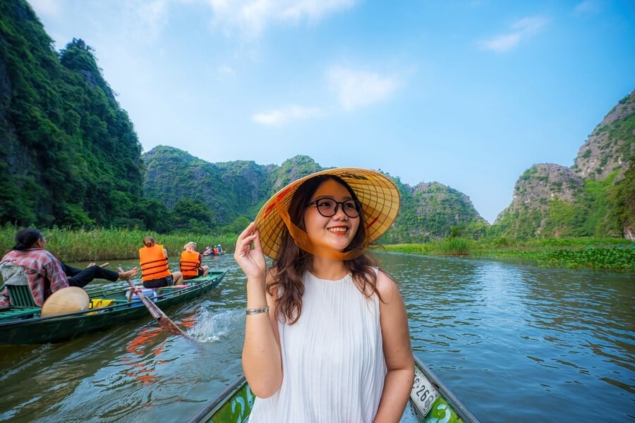Tourists on a boat rowed by local boatwoman along Ngo Dong River in Tam Coc, Ninh Binh, Vietnam