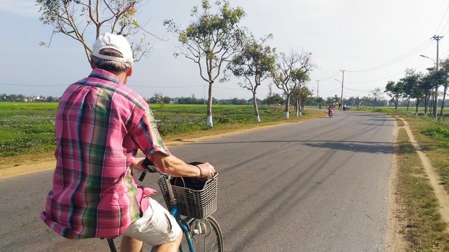 Tourist cycling leisurely along a rural path through rice fields in Vietnam, a common way to explore the countryside.