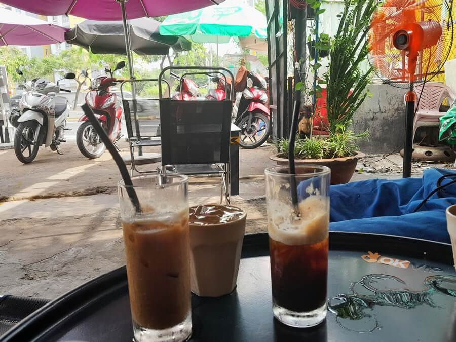 Two glasses of Saigon iced coffee on a table overlooking motorbikes parked outside