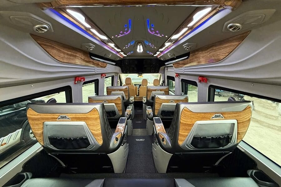 Wide VIP cabin interior of a luxury limousine van with reclining leather seats, LED ambient lighting and wood trim for private transport in Vietnam