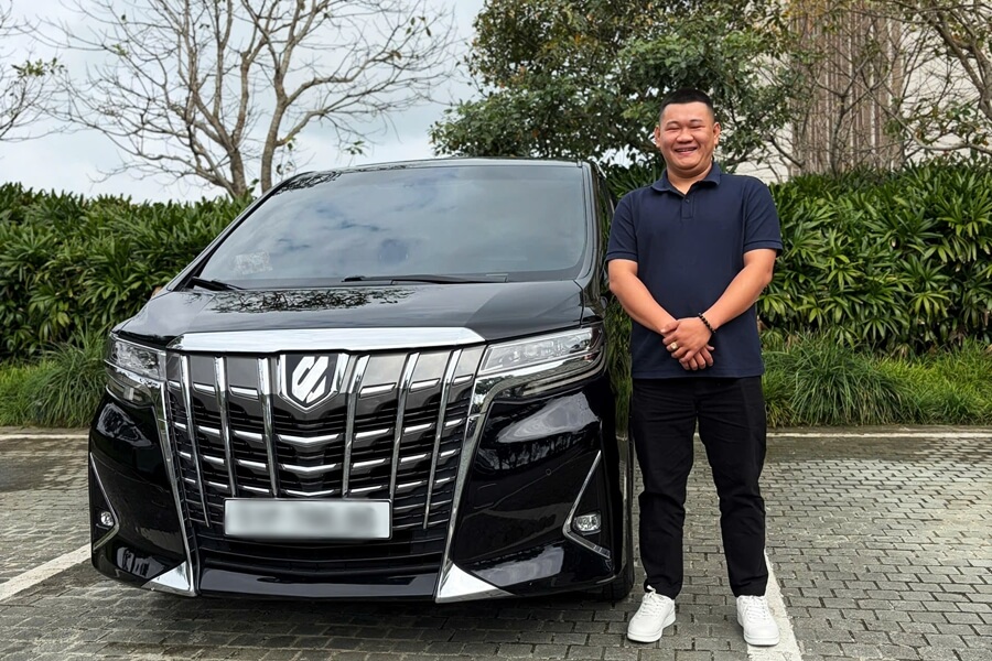 Professional chauffeur standing beside a black Toyota Alphard for luxury car service in Vietnam