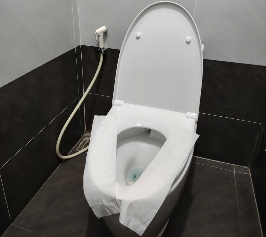 Toilet seat covered with toilet paper in a public toilet in Vietnam