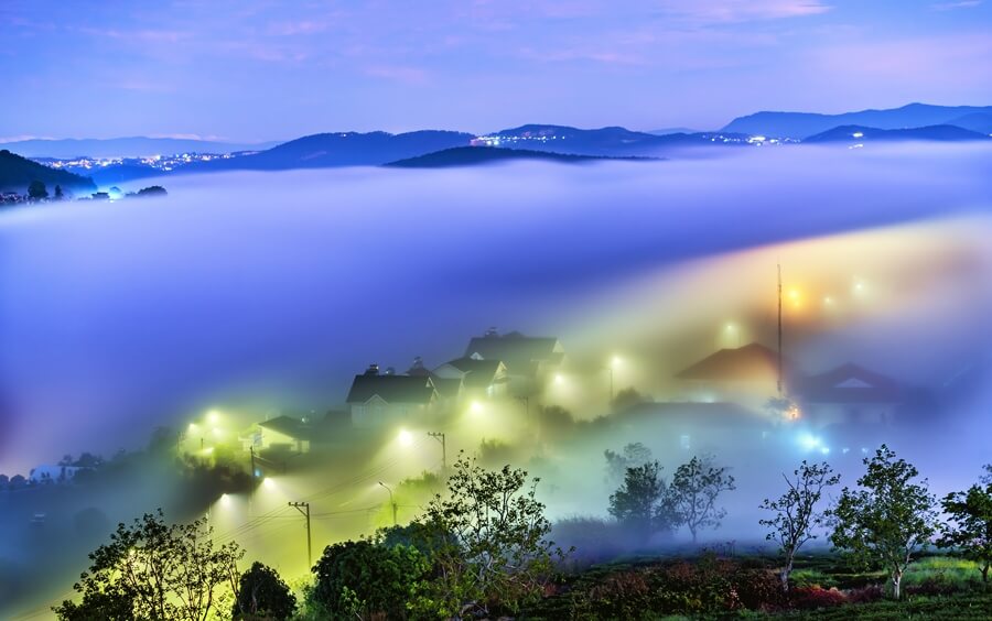 Street lights glowing through the morning fog near a lake in Da Lat, Vietnam