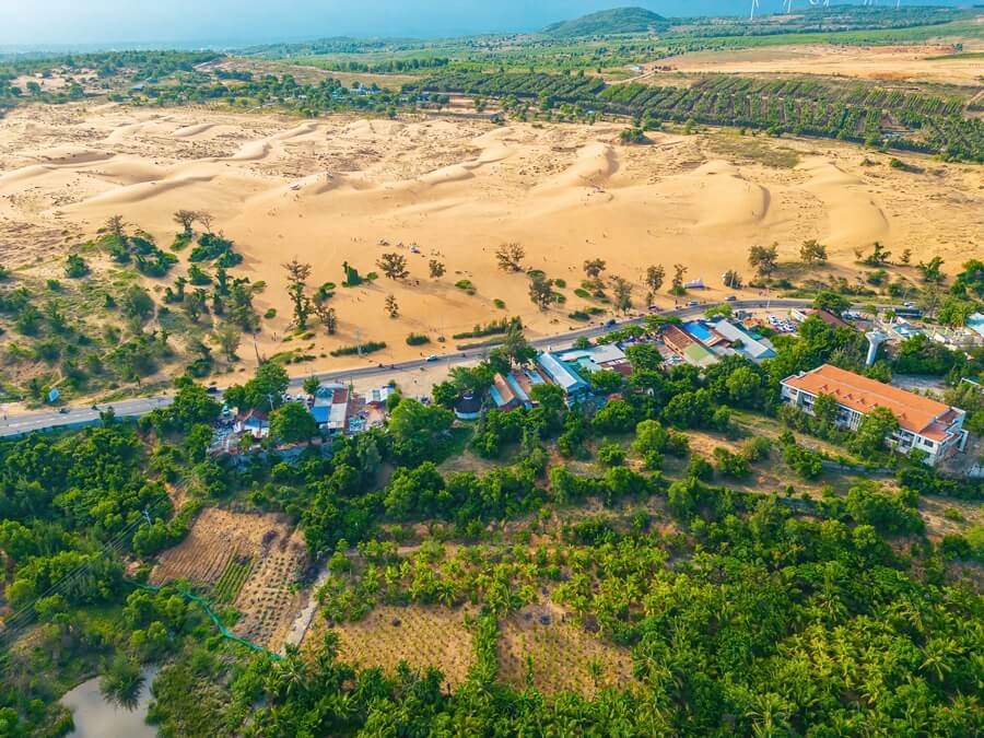 A road running between the sand dunes and green village landscape in Mui Ne, Vietnam
