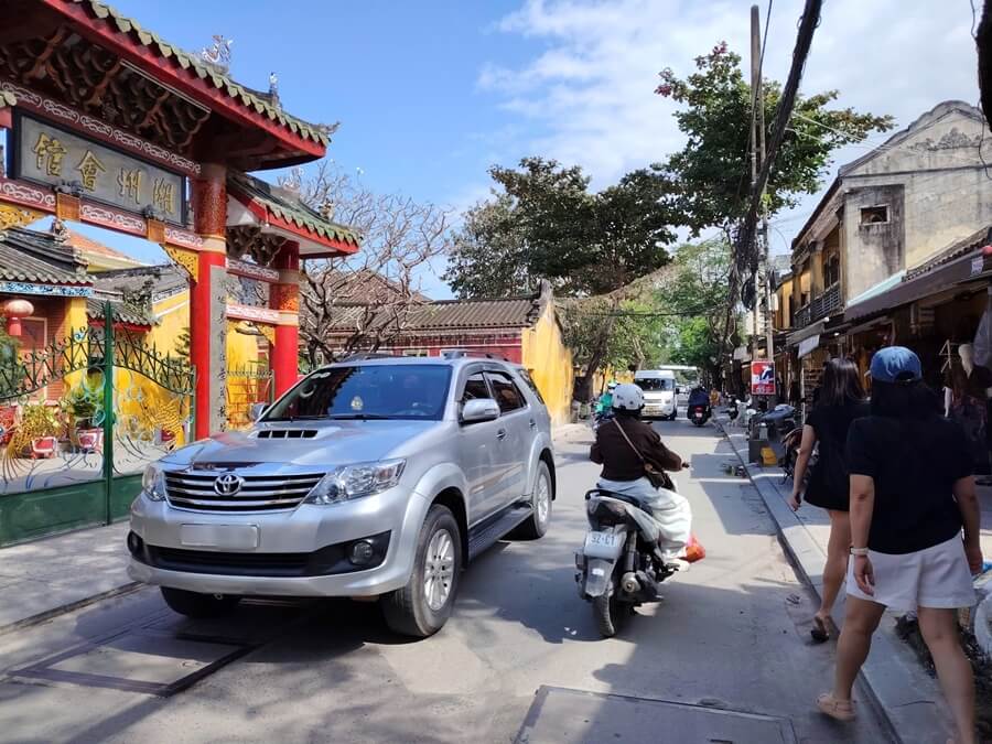A 7-seater private car driving along a narrow street near Hoi An Ancient Town